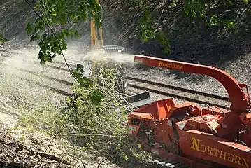 Brush being fed into a wood chipper next to a railway line
