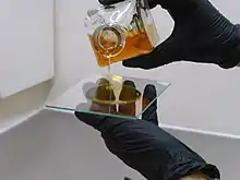 An artist wearing gloves pours liquid salt collodion onto a glass plate.