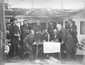 A posed photograph of Asiatic Squadron officers holding a council of war aboard USS&nbsp;Colorado off Korea in June 1871 prior to the Korean Expedition. Squadron commander Rear Admiral John Rodgers leans over the table at right.