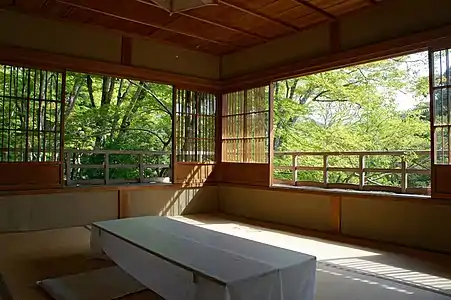 room with sliding screens at about 50&nbsp;cm height, looking out on the upper reaches of sunlit trees. The screens have a low wooden panel, and a high lattice which appears to be open but is actually glass-filled.