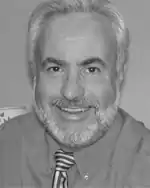 Black and white photo of a middle-aged man with gray hair and beard, wearing a dress shirt and necktie