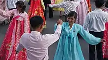 Women dressed in traditional outfits dance with men on the street.