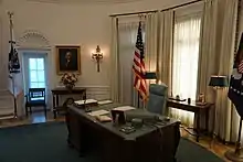  the desk viewed from slightly above showing the green top and the rest of the oval office behind it.
