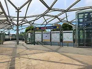 Photograph of station entrance at ground level, enclosed with a glass canopy. Other signs indicate the station name and locality maps.