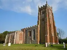 A bbuttressed rick tower with battlemented parapet, and the body of the flint church beyond