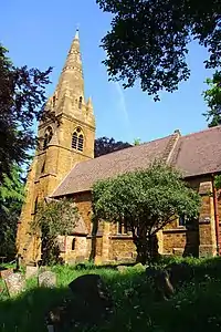 A stone church with a tiled roof; on the left is a tower with a tall spire, and the body of the church extends to the right