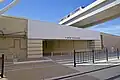 Pedestrian crosswalk and entrance to airport Terminal B. Just north of the platform, the DFW Skylink elevated track passes over the TEXRail tracks.