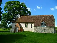 A small simple church, largely rendered with a tiled roof, a brick porch, and a bellcote at the west end
