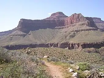 View of Tower of Set peak and sub-unit cliff section from Tonto Trail, Granite Gorge, north of Mohave Point, Grand Canyon Village, South Rim. The peak is behind and separated from a cliff unit (with small prominence), in front-(photo center, right, Tower of Set (peak) to its left). Vertical erosion in cliff of Redwall Limestone, upon horizontal Muav Limestone cliff. The Tapeats Sandstone sits in foreground on Granite Gorge,  and is seen as thinly-bedded. The slope-former above is the (dull-greenish)-Bright Angel Shale with thin, inter-bedding, as well as one resistant cliff unit. The Redwall Limestone cliff section in Grand Canyon is about 450 feet (137&nbsp;m) thick.